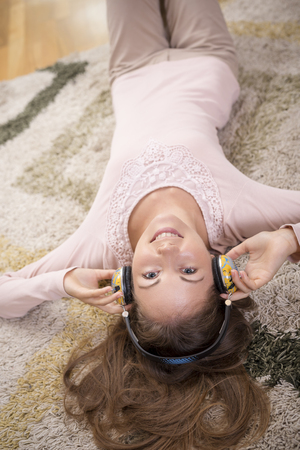 Top view of a beautiful brunette lying on the carpet on the floor of her apartment, listening to the music and enjoying her leisure timeの写真素材