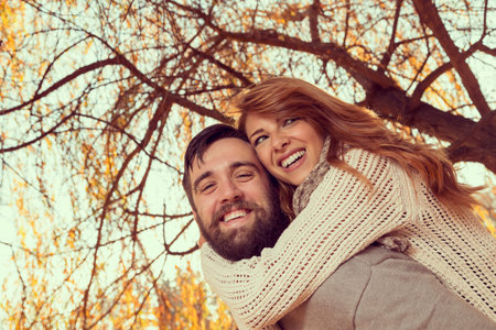 Couple in love having fun and fooling around on a wonderful autumn day in a park, guy piggybacking...