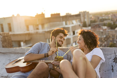 Young couple in love drinking a pineapple cocktail and having fun at rooftop party in sunset. Focus on the guyの写真素材