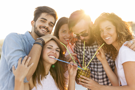 Group of young friends having fun at rooftop party, drinking a pineapple cocktail. Focus on the couple in the middleの写真素材