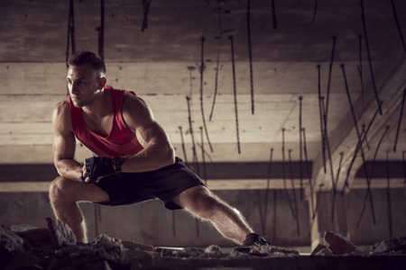 Muscular, athletic built, young man stretching out in a ruin building before workoutの写真素材