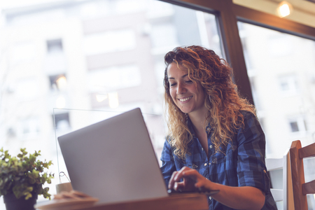 Beautiful young woman sitting in a coffee shop and working on a laptop computerの写真素材