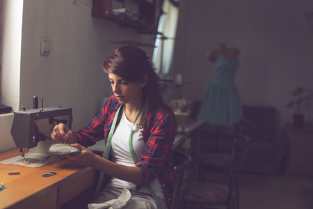 Young seamstress making some repairs, manually sewing in buttons on a shirtの写真素材