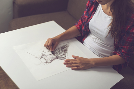 Detail of young fashion designer making a sketch of a new dress design. Focus on the charcoal in her handの写真素材