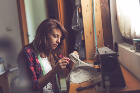 Young seamstress making some repairs, manually sewing in buttons on a shirt. Focus on the needleの写真素材