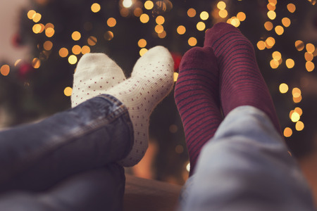Detail of male and female feet wearing warm winter socks, placed on the table with nicely decorated Christmas tree and Christmas lights in the background. Selective focusの写真素材
