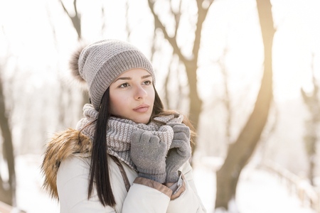 Beautiful young woman standing, holding her scarf and smiling, enjoying a beautiful snowy winter dayの写真素材