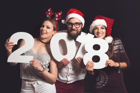 Three young friends having fun at New Year's Eve Party, holding cardboard numbers 2018