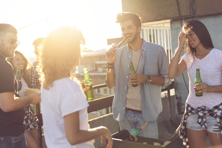 Group of young friends having fun at rooftop party, making barbecue, drinking beer and enjoying hot summer days.の写真素材