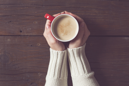 Top view of a female hands holding a cup of coffee on the wooden tableの写真素材