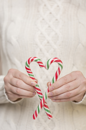 Detail of female hands holding two candy canes forming heart shape. Focus on the top of the candy caneの写真素材