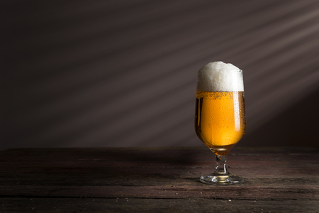 Glass of cold pale beer placed on a rustic wooden tableの写真素材