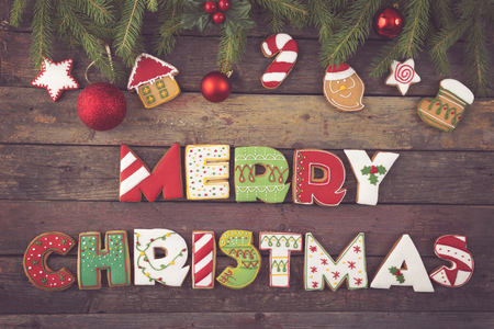 Table top shot of colorful gingerbread cookies shaped like letters Merry Christmas and Christmas tree decorations on fir tree branchesの写真素材