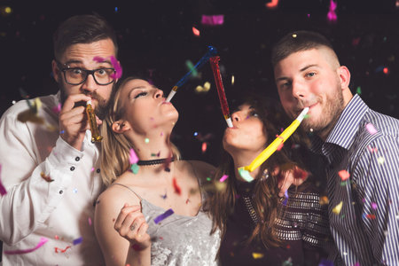 Two beautiful young couples having fun at New Year's party, dancing and blowing party whistles