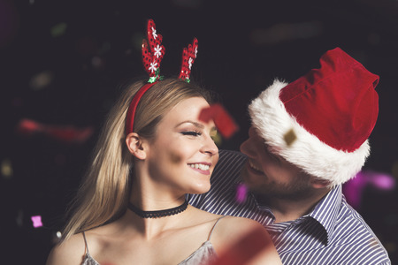 Couple in love wearing Santa's hat and antlers, dancing at a New Year's Eve party, kissing at midnightの写真素材