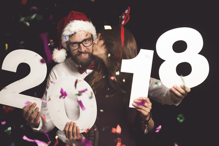 Young couple in love having fun at New Year's Eve party, holding cardboard numbers 2018の写真素材