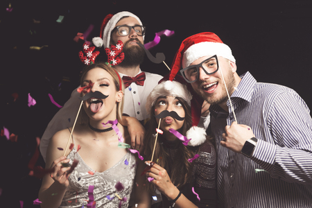 Four young friends having fun at New Year's Eve Party, posing for photos with masksの写真素材