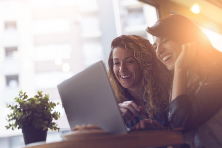 Two girls surfing the net, posting on social networks on a laptop computer and having funの写真素材