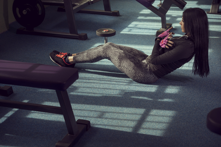 Attractive muscular young woman working out in a gym, doing sit ups on the floor next to a weightlifting machinesの写真素材