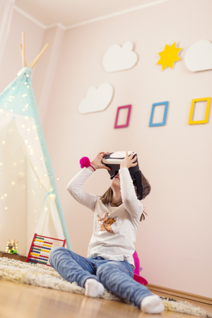 Little girl wearing virtual reality headset, playing in a playoom and having funの写真素材