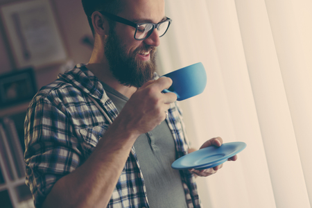Handsome man standing next to a window, drinking coffeeの写真素材