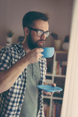 Handsome man standing next to a window, drinking coffeeの写真素材
