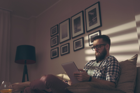 Handsome young man sitting on a living room sofa, having a video call with a friendの写真素材