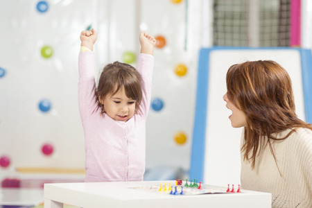 Mother and daughter sitting in a playroom, playing a ludo game; daughter happy because she won the gameの写真素材
