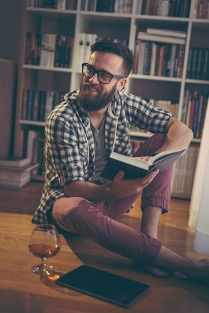 Young man enjoying his leisure time and relaxing while reading a book and having a drinkの写真素材