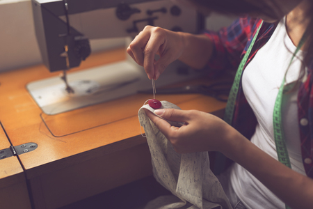 Young seamstress making some repairs, manually sewing in buttons on a shirt. Focus on the buttonの写真素材