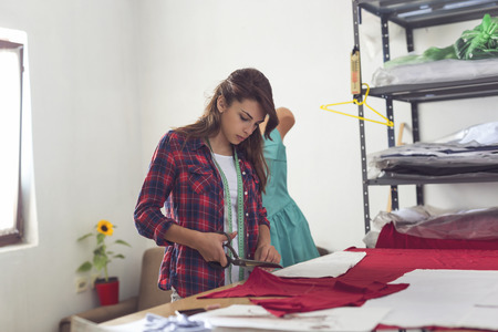Young seamstress cutting fabric with scissors, making new clothing models
の写真素材