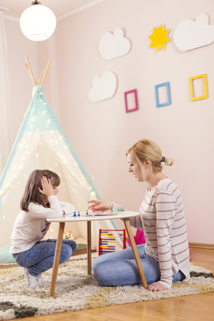 Mother and daughter sitting in a playroom, playing a ludo game and enjoying their time togetherの写真素材