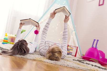 Mother and daughter lying on a playroom floor, reading books. Focus on the motherの写真素材
