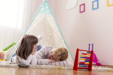 Mother and daughter lying on a playroom floor, speaking to each other and relaxing. Focus on the motherの写真素材