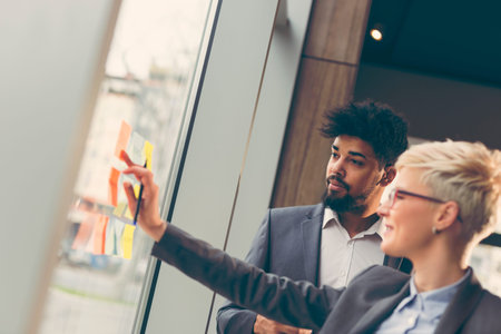 Businessman and businesswoman brainstorming using sticky notes on a glass wall in an office