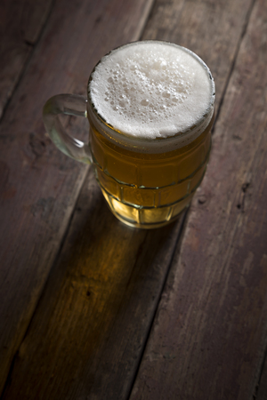 High angle view of a jug of cold pale beer placed on a rustic wooden table. Selective focus on the foamの写真素材
