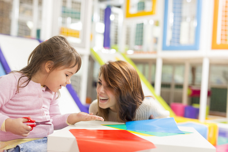 Mother and daughter sitting on a playroom floor, cutting colorful collage paper with scissors and having fun. Focus on the daughterの写真素材