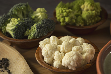 Fresh pieces of cauliflower, broccoli and romanesco broccoli in small rustic wooden bowls. Selective focus on the cauliflowerの写真素材