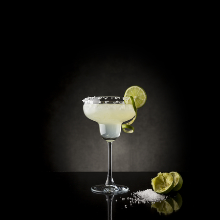 Classic lime margarita cocktail with tequila, triple sec, lime juice, crushed ice and some salt on the rim of a glass, decorated with a slice of limeの写真素材