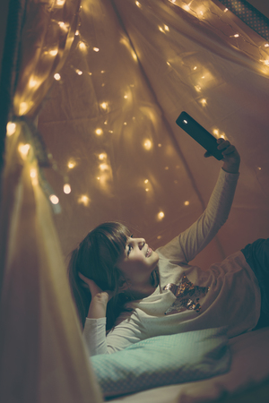 Little girl playing in a teepee, taking a selfie with smart phoneの写真素材