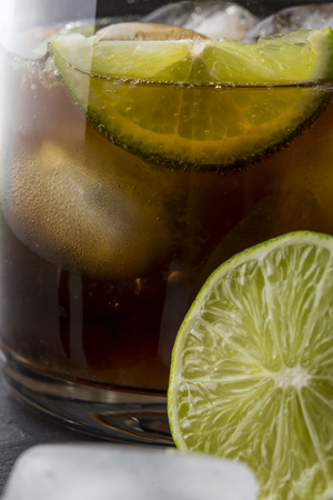 Close up of a glass of Cuba Libre cocktail with brown rum, lemon juice, coke and ice cubes, decorated with fresh lime slice. Selective focusの写真素材