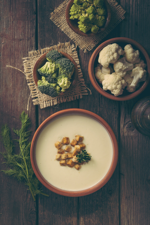 Table top shot of cauliflower soup decorated with parsley leaves and some croutons, with fresh vegetables around itの写真素材
