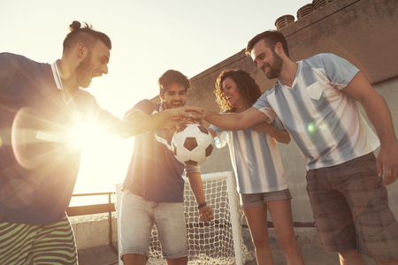 Group of young friends having fun playing football on a building rooftop, holding the ball before the match. Focus on the people in the middleの写真素材