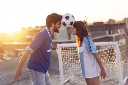 Young couple in love having fun on a building rooftop after playing football, dancing and balancing with the ball between their headsの写真素材