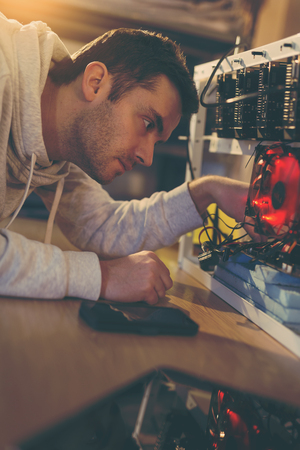 Young programmer adjusting cryptocurrency mining rig to optimal operational settingsの写真素材
