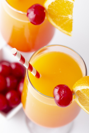 High angle view of two cold tequila sunrise cocktails with tequila, pomegranate juice and orange juice decorated with slices of orange and maraschino cherries. Focus on the cherry on the glassの写真素材