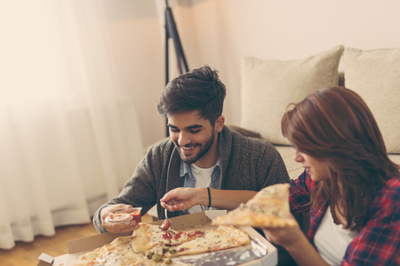 Young couple in love sitting on a living room floor, eating pica and having funの写真素材