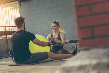 Couple sitting on a yoga mat on a building rooftop terrace, exercising with a pilates ballの写真素材