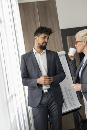 Two business people standing in a conference room, discussing work related matters while on a coffee breakの写真素材
