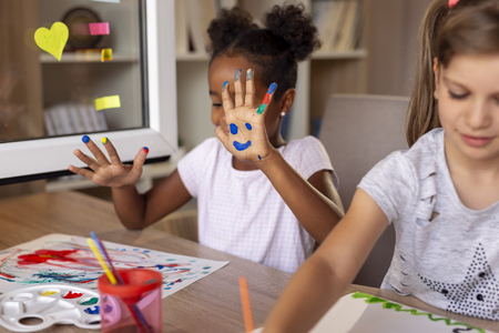 Beautiful little girls having fun painting with water colors, finishing their art class project. Focus on the smiley handの写真素材